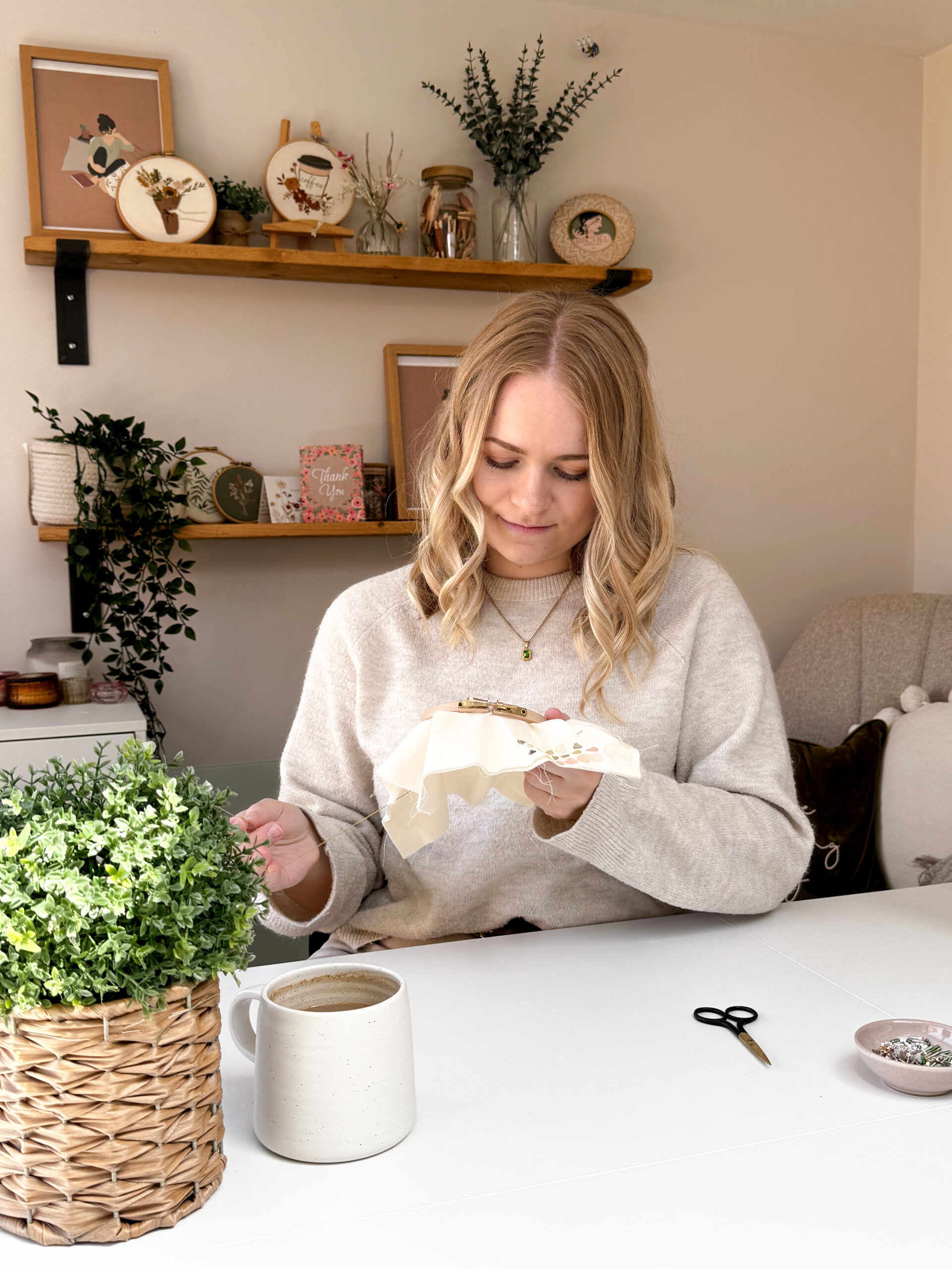 Sophie sat at her desk in her cosy studio, stitching an embroidery hoop with a mug of coffee close by.